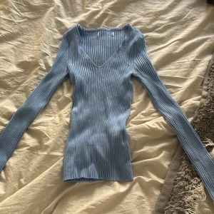 Ljusblå ribbad v-ringad tröja - Säljer en ljusblå ribbad tröja med v-ringning och lång ärm. Tröjan är figurnära och har en mjuk, stretchig känsla. Perfekt för lager-på-lager eller som den är till jeans eller kjol.