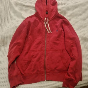 Polo Ralph Lauren zip hoodie  - Röd huvtröja från Polo Ralph Lauren med dragkedja och justerbar huva. Tröjan har en broderad logga i blått på bröstet och praktiska fickor framtill. Se bilder för skick. 