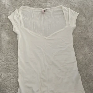 Vit kortärmad topp från Nelly - Säljer en söt vit topp från Nelly med korta ärmar och v-ringning. Toppen har fina spetsdetaljer längs halsringningen. Endast testad. 
