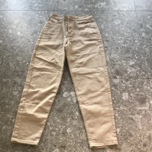 Beiga raka byxor från H&M - Säljer ett par beiga byxor från H&M med rak passform och klassisk femficksdesign. Byxorna har normal midja och är tillverkade i bomullsmaterial. Perfekta för en avslappnad och stilren look.