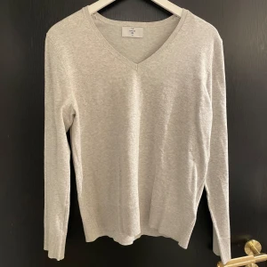Beige v-ringad tröja från The Basics - Säljer en stilren beige v-ringad tröja från The Basics. Tröjan har långa ärmar och ribbade kanter vid ärmslut och nederkant. Perfekt för en avslappnad look.