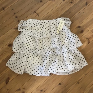 Vit prickig klänning med volanger - Söt vit klänning med svarta prickar och flera lager av volanger. Perfekt för en somrig look. Klänningen är elastisk.