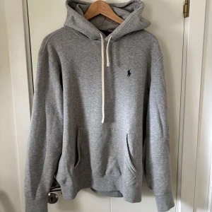 Ralph Lauren Hoodie - Säljer en stilren grå hoodie från Polo Ralph Lauren. Hoodien är i storlek M men passar storlek L mycket bättre! Endast använd fåtal gånger. Inga defekter, bra skick, vid frågor och funderingar är det bara att höra av sig:)
