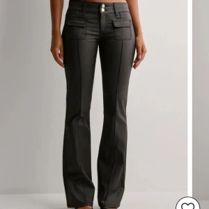 Svarta Skinnbyxor från Nelly  - Snygga svarta lågmidjade bootcut byxor med två knappar i midjan, en figurnära passform upptill och utsvängda nedtill. Använda en gång🥰priset går att sänka något om man köper fort🥰