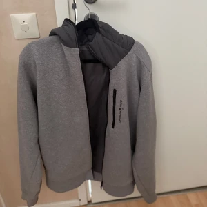 Grå jacka Sail Racing - Grå tunnjacka från Sail Racing med dragkedja och huva. Perfekt för lite kyligare dagar med sin stilrena design och praktiska fickor. Köpt på sailracing butiken för 1800, har dock inte använt den så många gånger för att den har varit för stor för mig. Pris kan diskuteras