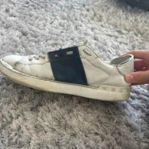 Valentino Open sneakers med blå detalj - Säljer ett par vita Valentino Open sneakers med en bred mörkblå panel över mitten. Skorna har rund tå, snörning och platt sula. Klassisk och stilren design med diskret Valentino-logga på plösen.
