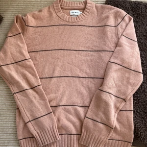 Rosa stickad tröja med svarta ränder från East West - Mysig rosa stickad tröja från East West i lammull. Tröjan har svarta tunna horisontella ränder och ribbade muddar vid ärmslut och nederkant. Perfekt för kyligare dagar och enkel att matcha med jeans.