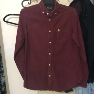 Vinröd skjorta från Lyle & Scott - Vinröd skjorta från Lyle & Scott med klassisk krage och vita knappar. Bröstficka med broderad gul logotyp. Skjortan har lång ärm och är i ett mjukt bomullsmaterial. Perfekt för dig som gillar stilrena detaljer.