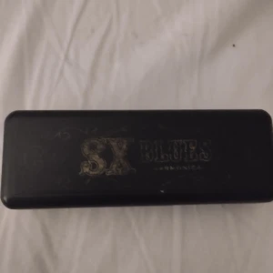 SX Blues munspel med etui - Säljer ett SX Blues munspel i metall med tillhörande svart plastetui. Perfekt för dig som vill spela blues eller annan musik. Munspelet har tydliga siffror och snygg gravyr på framsidan.