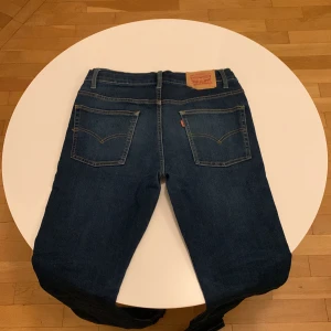 Mörkblå jeans från Levi's - Snygga mörkblå Levi's jeans med klassisk femficksdesign och knappgylf. Perfekta för en avslappnad stil. Märkeslappen i läder baktill ger en autentisk touch.