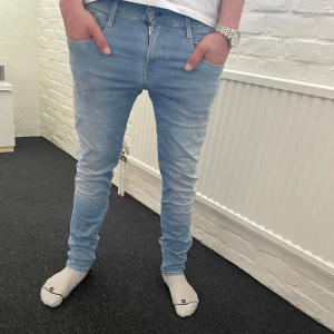 Replay anbass hyperflex jeans  - Snygga ljusblå jeans från Replay med en slim passform. De har en klassisk femficksdesign och en dragkedja med knappstängning. Perfekta för en stilren look. Storlek 30/32