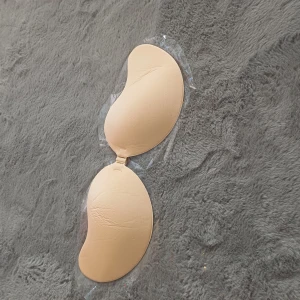 Beige självhäftande bh - Säljer en beige självhäftande bh utan axelband. Perfekt för klänningar och toppar med öppen rygg. Den har en slät yta och en praktisk knäppning framtill för justerbar passform.