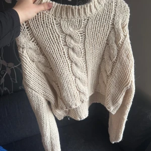 Beige stickad tröja med flätmönster - Säljer en chunky beige stickad tröja med grovt flätmönster framtill. Tröjan har lång ärm, rund halsringning och är perfekt för kyliga dagar. Supermysig och passar till allt!