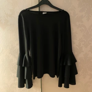 Festblus från Gina Tricot✨ - Säljer denna super söta svarta långärmade topp från Gina Tricot med snygga volang ärmar. Perfekt för dig som vill ha något stilrent men ändå med en twist. Passar perfekt till fest!