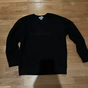 Svart sweatshirt från Moncler - Svart sweatshirt från Moncler med diskret logga framtill. Klassisk rund halsringning och långa ärmar. Perfekt för en stilren och enkel look.
