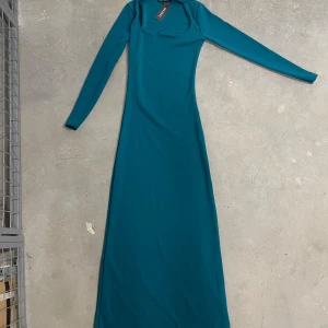 Petrolblå långklänning från Boohoo - Säljer en stilren petrolblå långklänning från Boohoo med lång ärm och fyrkantig ringning. Klänningen har en figurnära passform och är tillverkad i ett mjukt, stretchigt material som ger en snygg siluett.