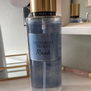 Victoria's Secret Rush Body Mist - Fräsch body mist från Victoria's Secret i doften Rush. Flaskan är genomskinlig med blå etikett och gulddetaljer. Doften har inslag av sensuella tränoter och mandarin, perfekt för dig som gillar fruktiga och träiga toner. Knappt använd så nästan hela kvar. 