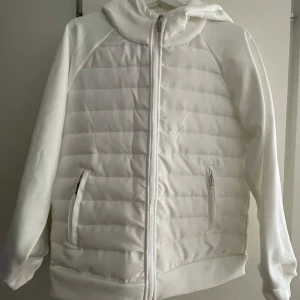Vit pufferjacka / vårjacka med huva - Snygg vit pufferjacka / vårjacka med dragkedja framtill och två fickor med dragkedja. Helt oanvänd. Köpt från Verani i april 2025 men fel storlek. 