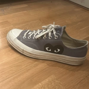Converse Play x Comme des Garçons sneakers grå - Grå Converse Play x Comme des Garçons sneakers med det ikoniska hjärta-ögon-trycket på sidan. Skorna har vit tå, vita snören och sula, samt klassisk låg modell. Perfekta för dig som gillar streetwear och vill sticka ut lite extra. Skorna är knappt använda.