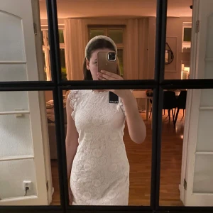 Vit spetsklänning - Elegant vit klänning i spets med korta ärmar och rund hals. Perfekt för en stilren look med vackra spetsdetaljer som ger en romantisk känsla. Helt ny med prislapp, aldrig använd