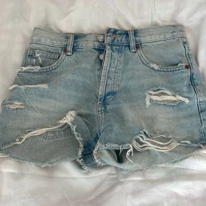Ljusblåa slitna jeansshorts från ZARA - Ljusblåa jeansshorts från ZARA med medel hög midja och flera slitningar framtill. Perfekt till sommaren.