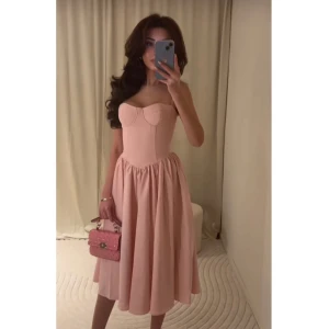 Rosa axelbandslös klänning - Elegant rosa axelbandslös klänning med en vacker, utsvängd kjol. Perfekt för speciella tillfällen med sin feminina och stilrena design.