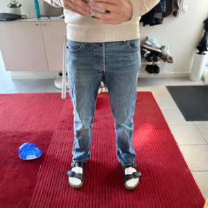 Blå jeansbyxor - Säljer ett par klassiska blå jeansbyxor med normal passform. De har en rak stil och är perfekta för en avslappnad look. Byxorna har fem fickor och en dragkedja framtill.