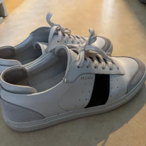Vita sneakers från Axel Arigato - Snygga vita sneakers från Axel Arigato med en svart detalj på sidan. Skorna har endast blivit använda vid 3-4 tillfällen. Priset är diskuterbart.