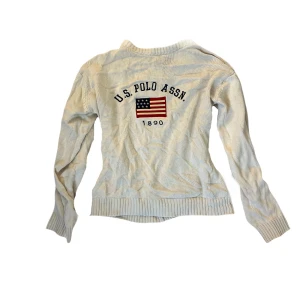 Vit tröja från U.S. Polo Assn. - Säljer en vit/beige tröja från U.S. Polo Assn. med ett tryck av den amerikanska flaggan och texten 'U.S. Polo Assn. 1890' i fram. Tröjan har långa ärmar och ribbstickade muddar vid ärmslut och nederkant. Tröjan har ett litet hål på sidan men det syns knappt. Den passar mig som brukar ha S men den är egentligen L! Pris kan diskuteras 💞
