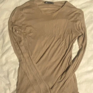 Beige långärmad topp från Zara - Säljer en stilren beige långärmad topp från Zara. Enkel och mångsidig design som passar till många olika outfits. Har aldrig använt den. Toppen är lite genomskinlig. Kvaliten är superbra. Priset kan diskuteras.