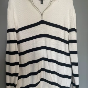 Vit och svart randig tröja från H&M - Säljer en stilren vit och svart randig tröja från H&M. Tröjan har en dragkedja vid halsen och är långärmad med en slim fit passform. Perfekt för en avslappnad men snygg look.