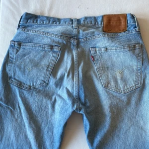 Ljusa 501 jeans från Levi's  - Säljer ett par klassiska ljusa Levi's jeans med fem fickor och en knappgylf. De har en traditionell passform och är perfekta för en avslappnad stil. Levi's logotyp syns på den bruna läderpatchen baktill. Dem är lite större i storleken.