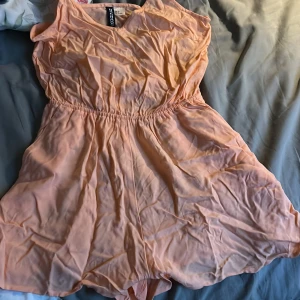 Persikofärgad klänning från H&M Divided - Säljer en söt persikofärgad klänning från H&M Divided. Klänningen är ärmlös med en elastisk midja för en bekväm passform. Perfekt för varma dagar!