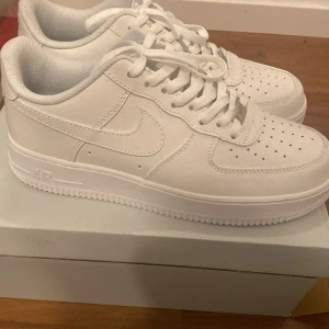Vita Nike Airforce One - Säljer ett par klassiska vita Nike Air Force sneakers. Skorna har en stilren design med snörning och perforerade detaljer på tån för extra ventilation. Perfekta för en casual look. Aldrig använda och därför jag säljer dem. OBS SKRIV INNAN KÖP! Pris går såklart att diskutera