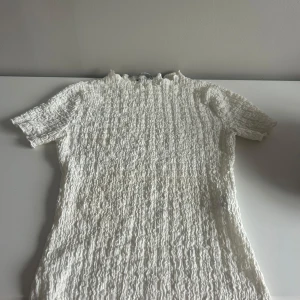 Vit ribbad topp - Säljer en stilren vit ribbad topp med korta ärmar och hög krage. Perfekt för en chic och enkel look. Passar bra till både jeans och kjol.