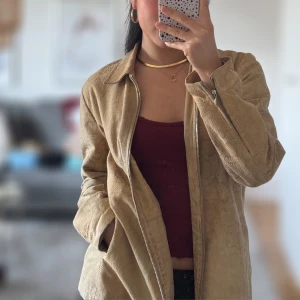 Beige jacka med ormskinnsmönster - Snygg beige jacka med ormskinnsmönster och dragkedja framtill. Jackan har långa ärmar och en klassisk krage. Perfekt för att ge en trendig touch till din outfit. 100% real leather