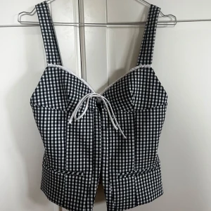 Rutig korsett topp Zara - Säljer denna rutiga korsett topp från Zara. Helt oanvänd. Vitt och mörkblått rutigt mönster med korsett hakar framtil och knytning. Storlek XS. Perfekt nu till våren.