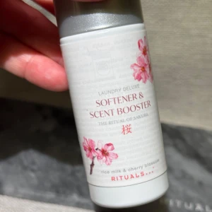 Ny! The Ritual of Sakura Softener & Scent Booster - Nytt sköljmedel 75ml. Upptäck en lyxig doftförstärkare och mjukmedel från Rituals, The Ritual of Sakura. Denna produkt kombinerar doften av ris-mjölk och körsbärsblomma för en fräsch och upplyftande tvättupplevelse. Förpackningen är vit med rosa blommotiv och en silverfärgad kork.