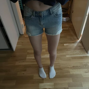 Jeansshorts med spetsdetaljer från Lindex - Snygga jeansshorts från Lindex med spetsdetaljer vid benen. De har en klassisk blå tvätt och fransiga kanter, perfekt för en sommardag. Skriv vid frågor.
