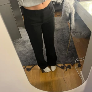 Svarta kostymbyxor från Nelly - Snygga svarta kostymbyxor med låg midja och rak passform. Perfekta för en stilren look. Byxorna har en dragkedja framtill och är tillverkade i ett klassiskt kostymmaterial.