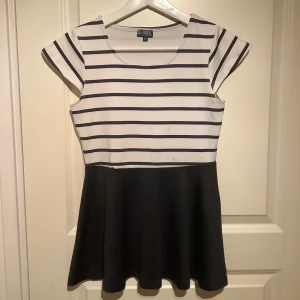 Randig klänning från D-XEL - Säljer en söt  topp från D-XEL med randigt mönster upptill och enfärgad utsvängd volang. Toppen har korta ärmar och en rund halsringning. Perfekt för en avslappnad stil.