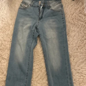 Ljusblå jeansbyxor passar ochså som xs/34 - Säljer ett par ljusblå jeansbyxor med normal passform. Byxorna har en klassisk femficksdesign med knappar och dragkedja framtill. Perfekta för en avslappnad stil.