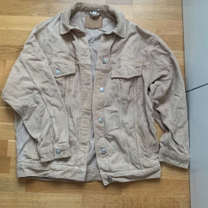 Beige manchesterjacka från Topshop - Säljer en snygg beige manchesterjacka från Topshop. Jackan har en klassisk krage, knappar framtill och två bröstfickor med knappar. Perfekt för en avslappnad stil.