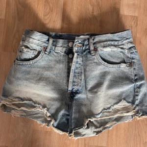 Jeansshorts med slitna detaljer - Säljer ett par coola jeansshorts med slitna detaljer och fransar. De är medelmidjade och har en klassisk blå denimfärg. Perfekta för en avslappnad sommarlook!
