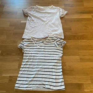 Två randiga t-shirts - Säljer två randiga t-shirts i bomull. Den ena är vit med tunna rosa ränder och den andra är vit med svarta ränder och v-ringning. Båda har korta ärmar och är perfekta för en avslappnad stil.