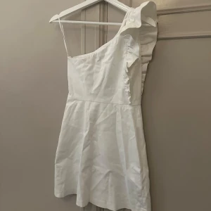 Vit axelbandslös klänning - Säljer en stilren vit klänning med en unik oneshoulder-design och volangdetalj. Perfekt för sommarens festligheter. Passar även bra som studentklänning 🤍Kontakta mig för fler bilder 💛