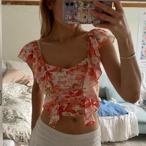 sommartopp med volanger!! - Så söt sommartopp med volanger i axlarna! Superfint rosablommigt mönster, passar till jeans eller kjol💕använd en gång