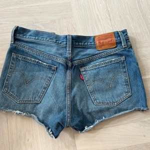 Blå jeansshorts från Levi's - Säljer ett par klassiska blå jeansshorts från Levi's med fransiga kanter och knappgylf. Lågmidjade super fina! Storlek 29, midjemått 82, modell 501!