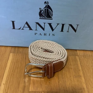 Beige flätat bälte - Snyggt beige flätat bälte med bruna skinninslag och en stilren metallspänne. Perfekt för att ge en touch av elegans till din outfit. Passar både till jeans och mer formella byxor. Helt nytt! 