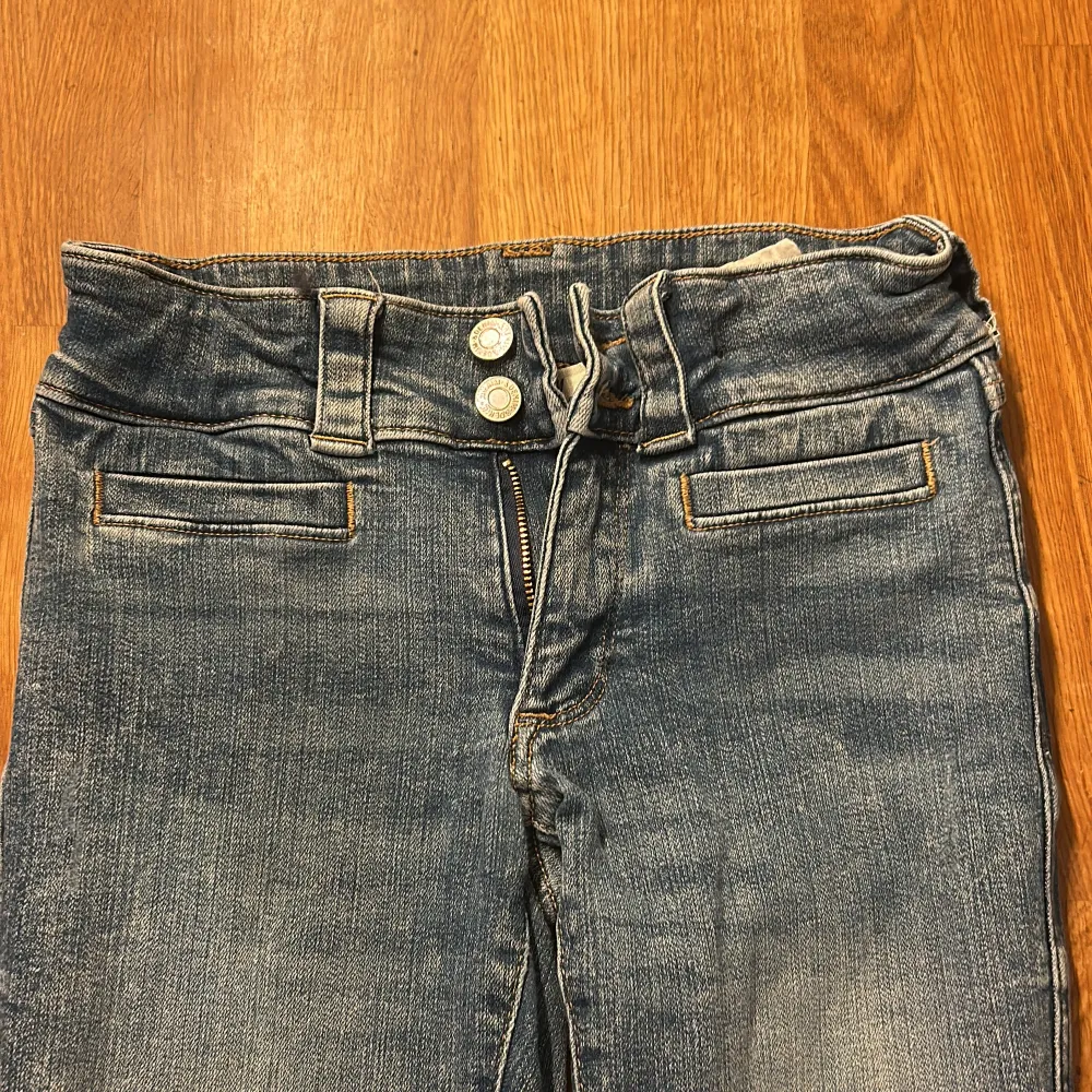 Snygga blå bootcut jeans med två knappar och dragkedja fram. De har fickor med lock och knappdetaljer bak. Perfekta för en avslappnad stil. Kom med förlag om pris ifall de inte passar.. Farkut & Housut.